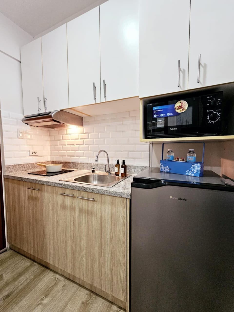 Fully equipped kitchen with stovetop, ref, microwave, rice cooker, water kettle.
