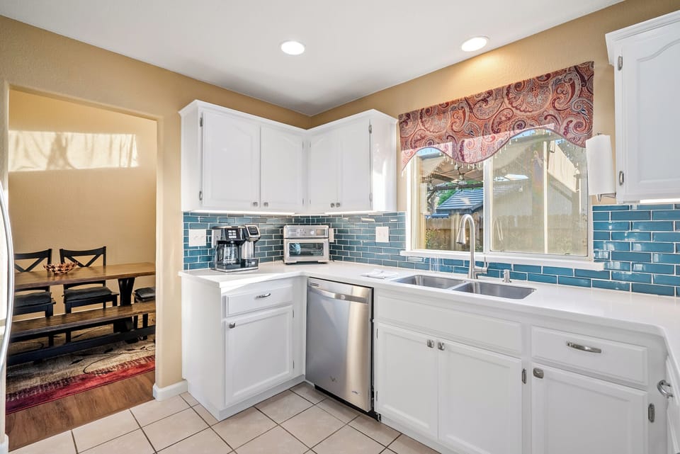 A bright and modern kitchen featuring vibrant blue subway tile backsplashes, crisp white cabinetry, and a sink-side window offering a view of the outdoors.