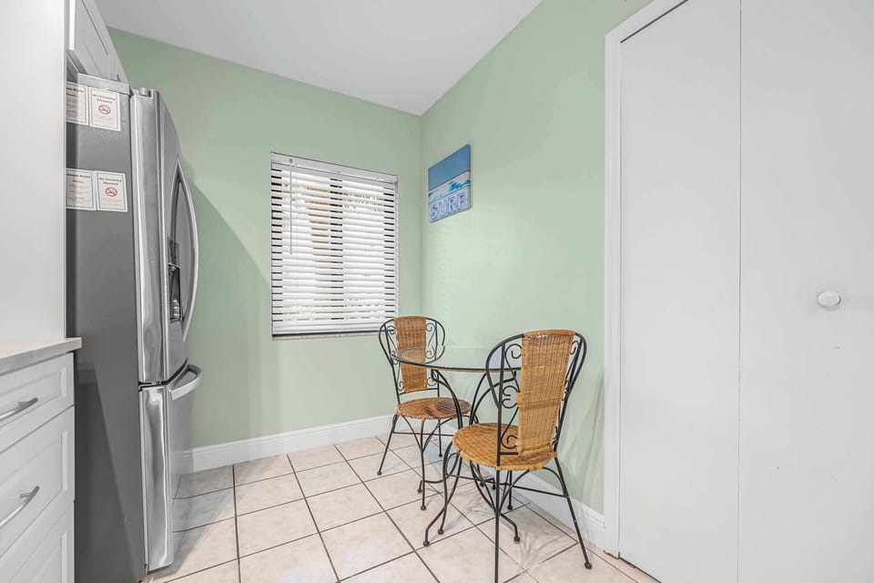 Cozy breakfast nook with a glass table and wicker chairs next to a stainless steel refrigerator.