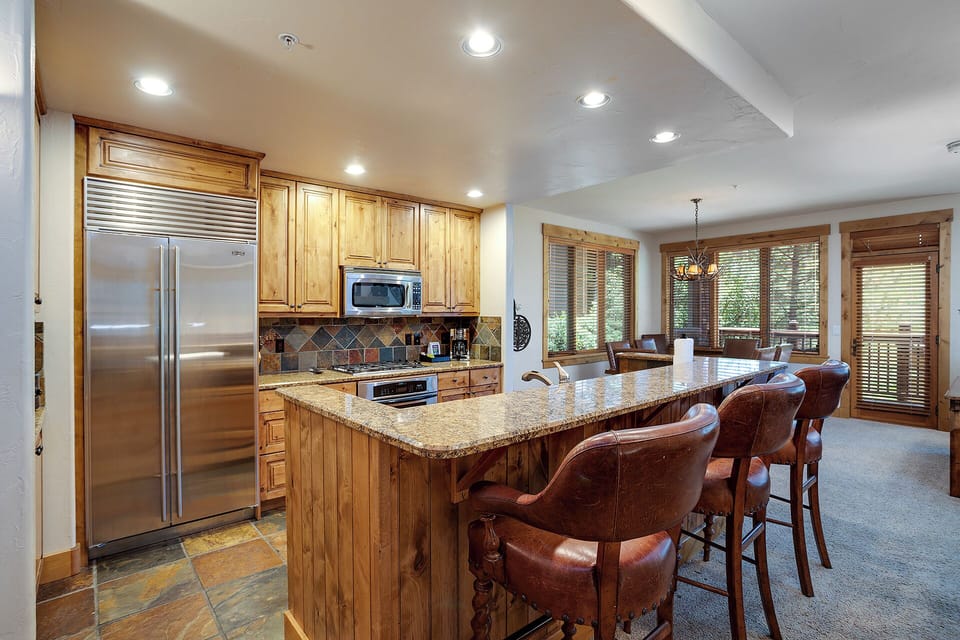 Gather around this stunning granite-topped kitchen island where warm wood cabinetry meets stainless steel appliances for your perfect culinary retreat.