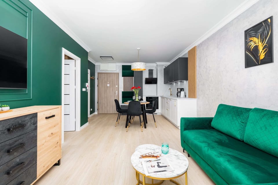 Wide view of the open living and dining area, showcasing the green sofa and modern furnishings.

