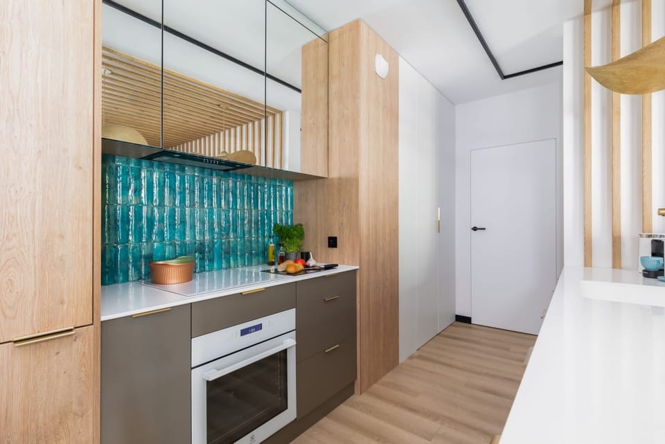 Fully equipped kitchen with bold teal tiles, modern appliances, and natural wood cabinetry.

