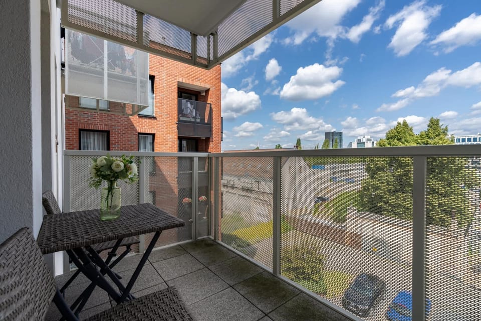 Balcony with a small table and chairs, overlooking a well-maintained residential area.

