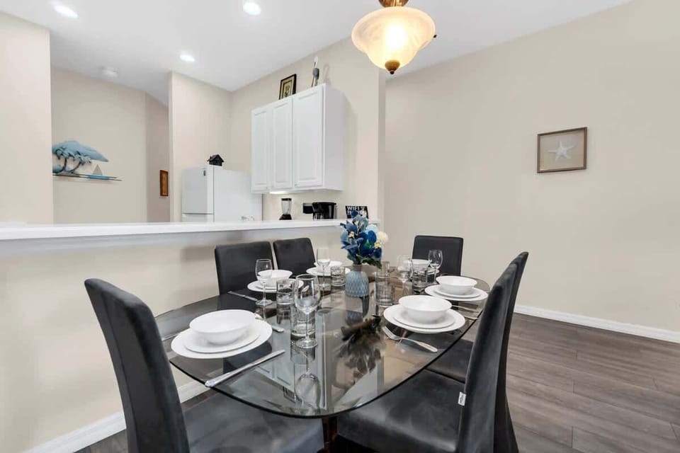 Modern dining area with a glass table set for six and an open kitchen view.
