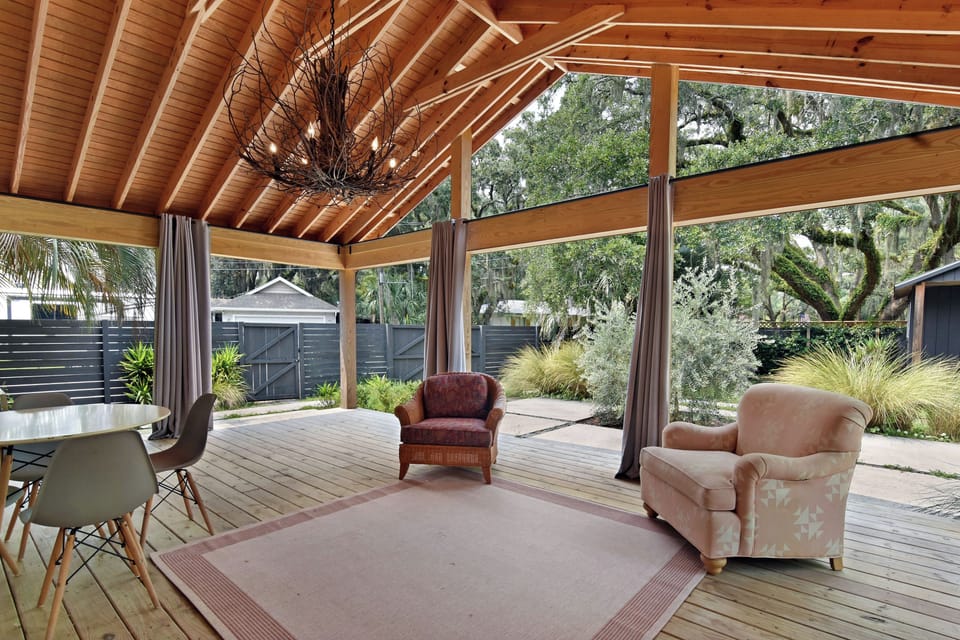 Covered Patio and Fenced Yard - Vaulted covered patio with lounge seating, ceiling fan, chandelier, curtains, and view into the fenced yard.