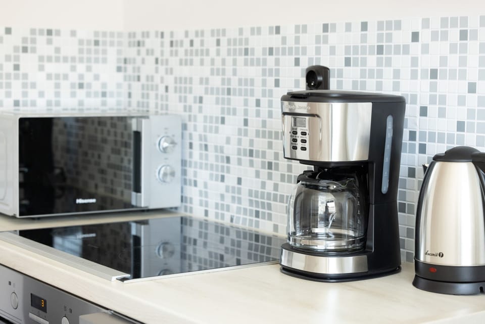 Well-equipped kitchen featuring a coffee maker, kettle, and mosaic-tiled backsplash.

