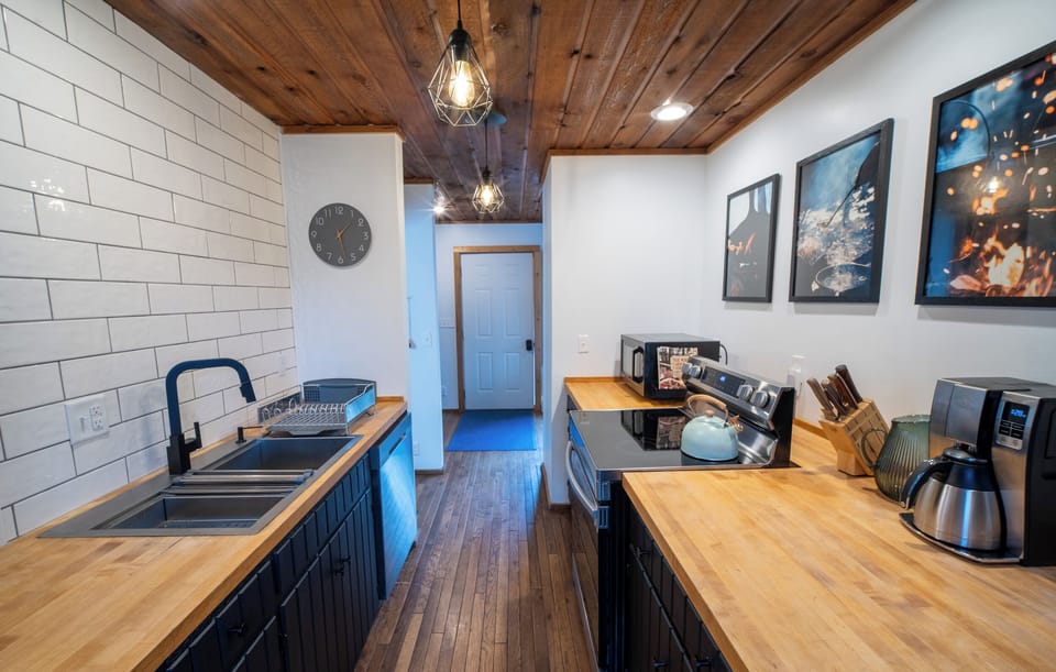 Modern galley kitchen with dark cabinets, butcher block countertops, stainless steel appliances, and a vaulted wood ceiling.