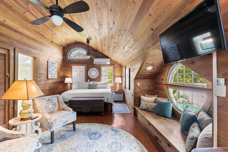 Third floor primary suite with vaulted wood ceilings, comfortable seating, a king bed, and beautiful architectural details.