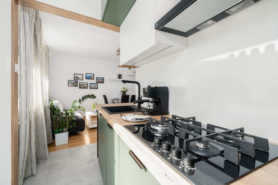 Bright kitchen with green accents, sleek appliances, and a window overlooking greenery.


