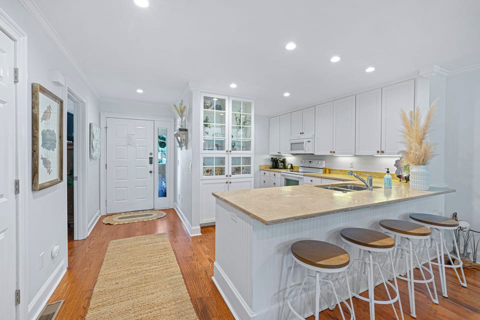 Clean, coastal kitchen with ample prep space and bar seating—flowing seamlessly from the entry into a bright, open layout designed for easy living and gathering.