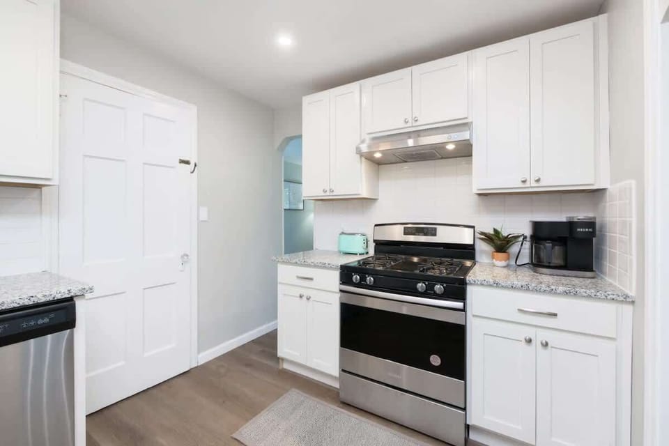 - Kitchen with granite countertops and stainless steel stove   - White cabinets and coffee maker for a complete cooking setup   - Bright lighting and clean design enhance modern functionality  