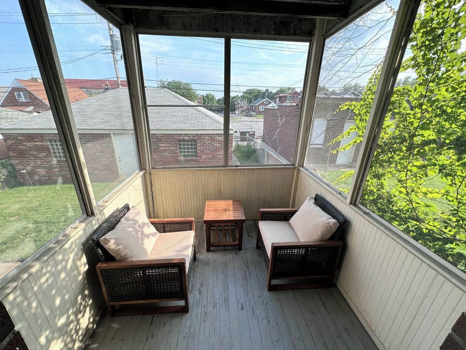 The screened porch provides two cushioned wood chairs, a small wood table, and views over the rear lawn and neighboring homes.