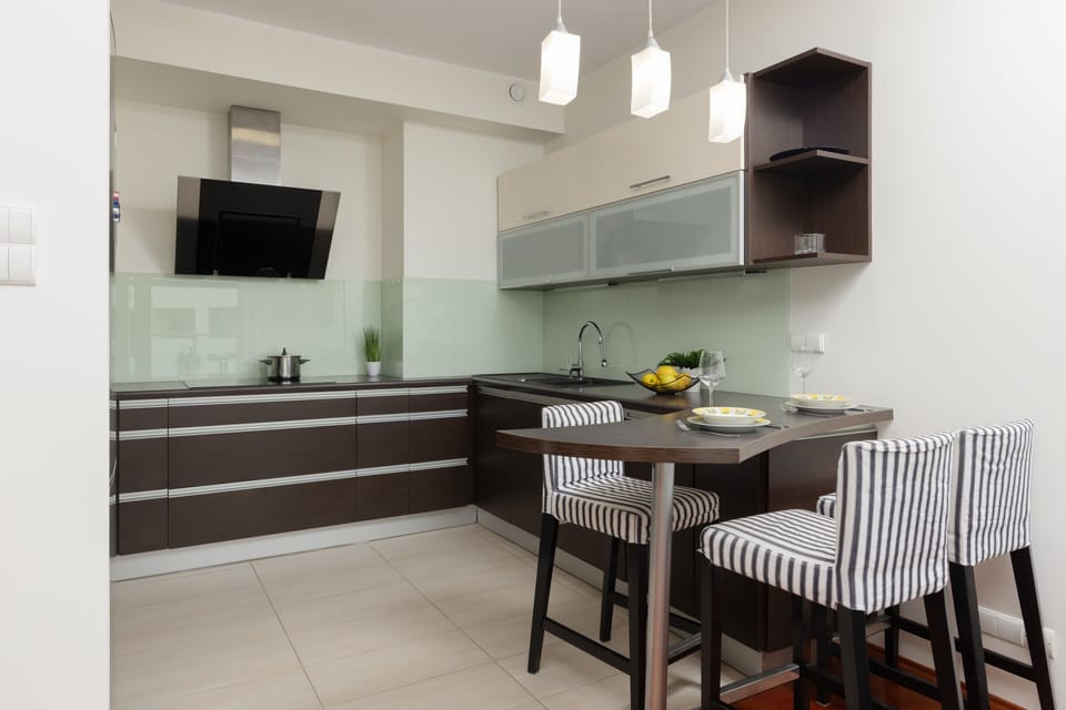 A kitchen with modern cabinetry, integrated appliances, and a dining table with striped chairs.

