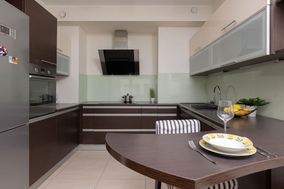 A sleek kitchen with dark cabinets, glass backsplash, and a wooden dining table set for two.

