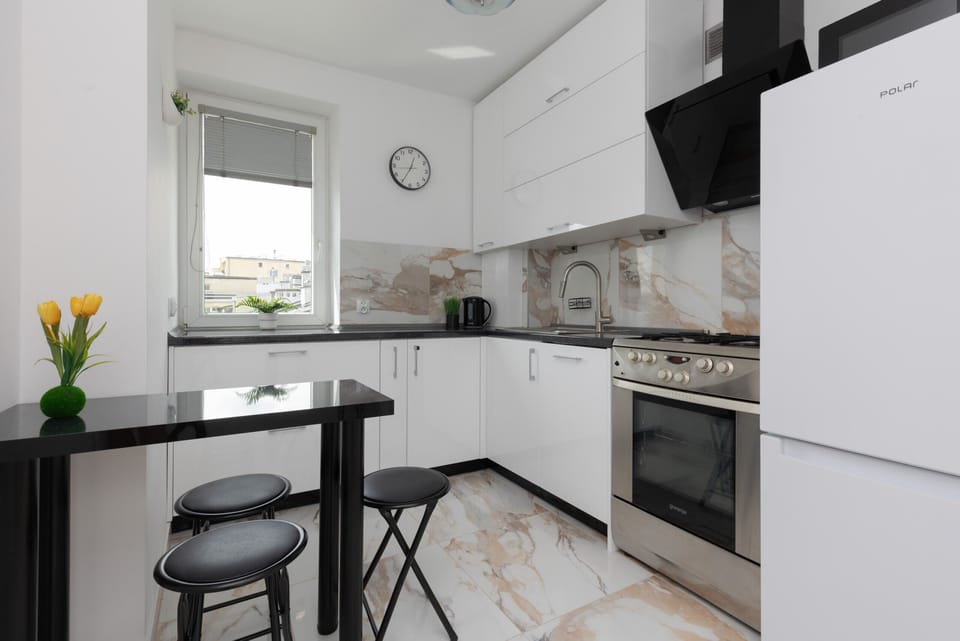 A modern kitchen with white cabinetry, a marble backsplash, and black bar stools for casual dining.

