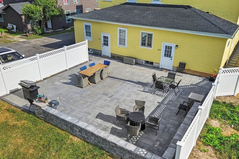 A sun-kissed yellow house, nestled in an open and spacious setting, features a welcoming porch adorned with comfortable seating.
