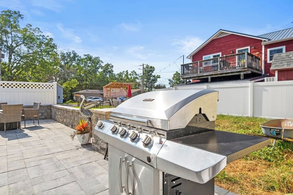 A sun-kissed yellow house, nestled in an open and spacious setting, features a welcoming porch adorned with comfortable seating and grill for your bqq nights.