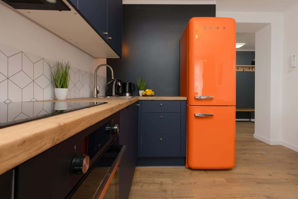 A kitchen with a wooden countertop, orange fridge, and dark cabinetry creating a bold, modern look.

