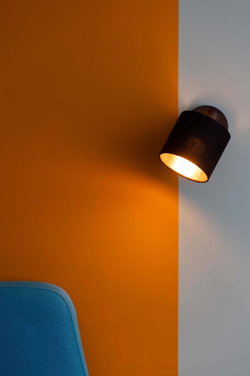 A close-up of a wall-mounted black lamp against a bright orange accent wall.

