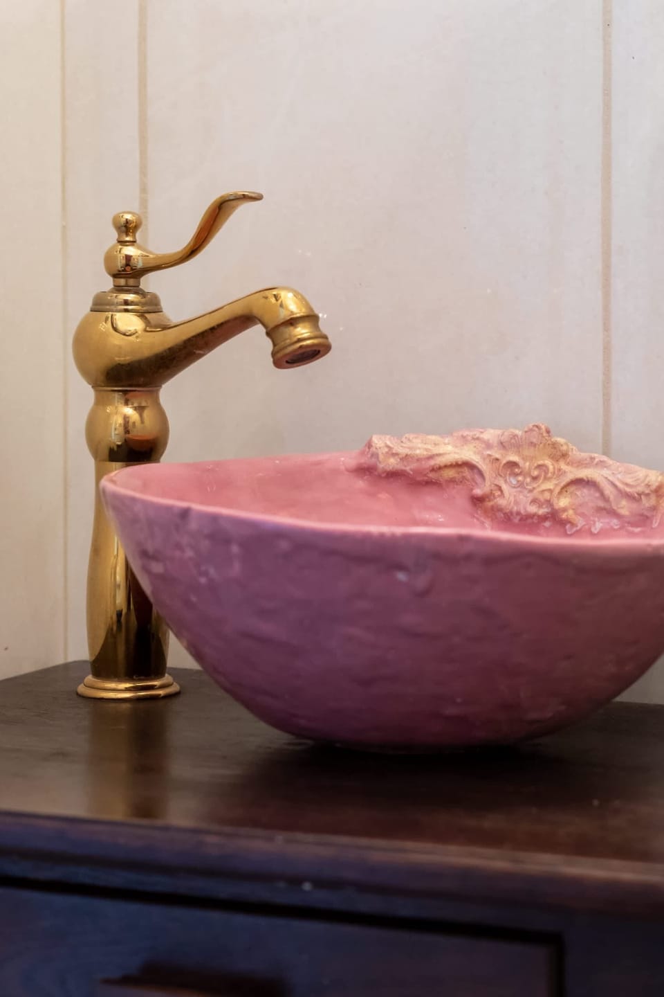 A close-up of a pink sink with a gold faucet, blending elegance with a bold design.

