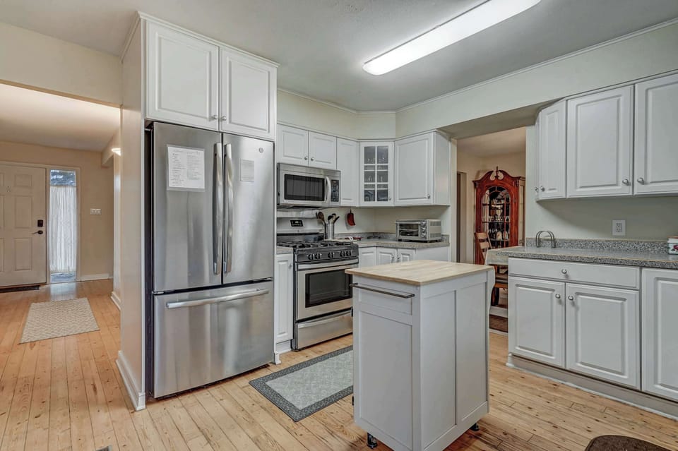 Bright kitchen features white cabinetry, stainless steel refrigerator, and a central island that brings everything together, making it easy to prep meals, lay out snacks, or gather casually while cooking.