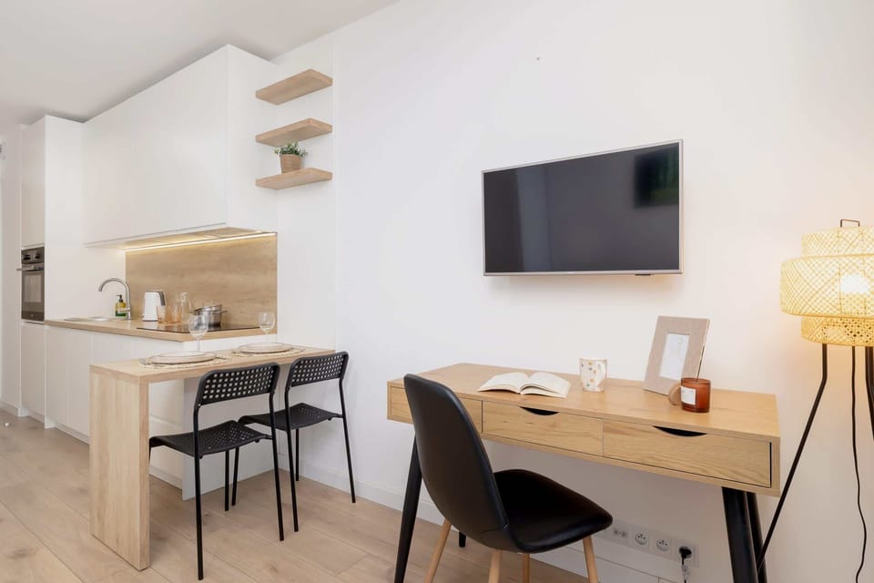 A dining and working area with a wooden table, black chairs, and open shelving in a bright space.

