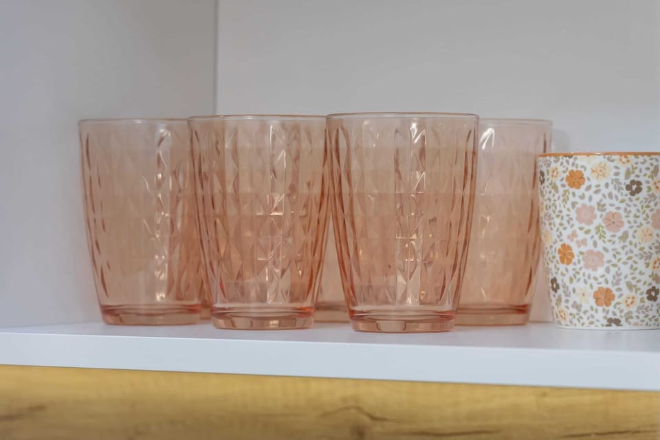A close-up of elegant pink glasses on a kitchen shelf, adding a decorative touch.


