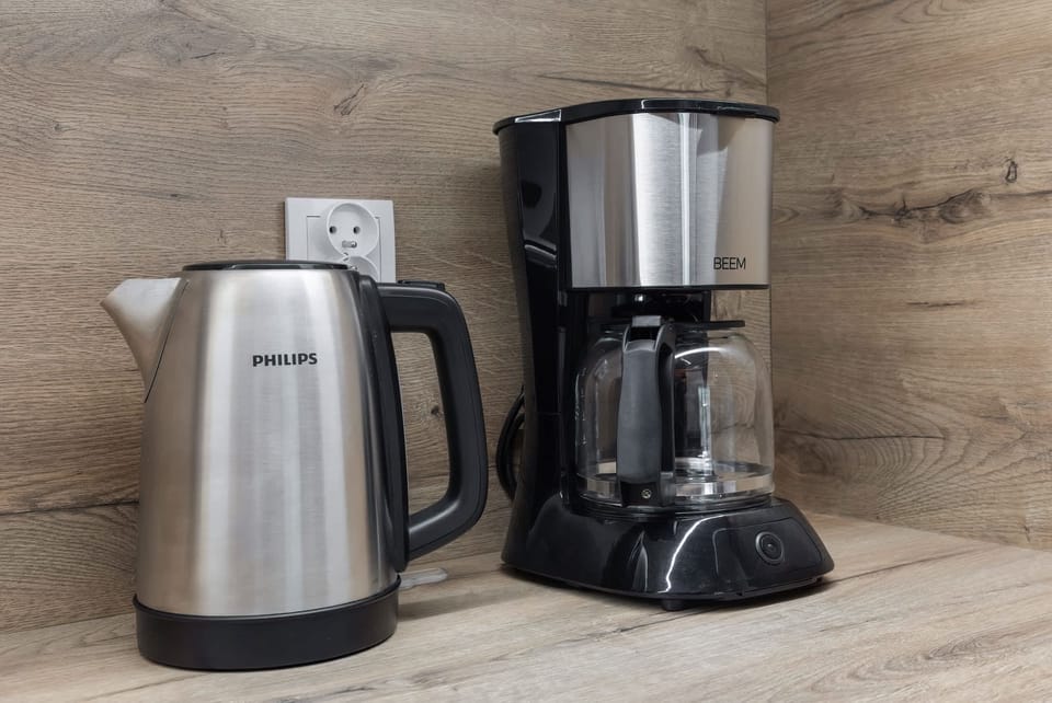 A coffee and tea station with a sleek electric kettle and coffee maker set on a wooden countertop for a convenient morning routine.

