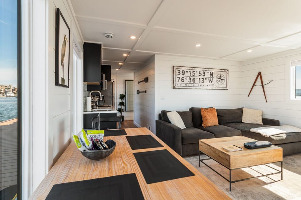 Open-concept main level with the four-seat dining table flowing into the sectional living area, anchored by the `Go With The Flo` coordinates wall art.