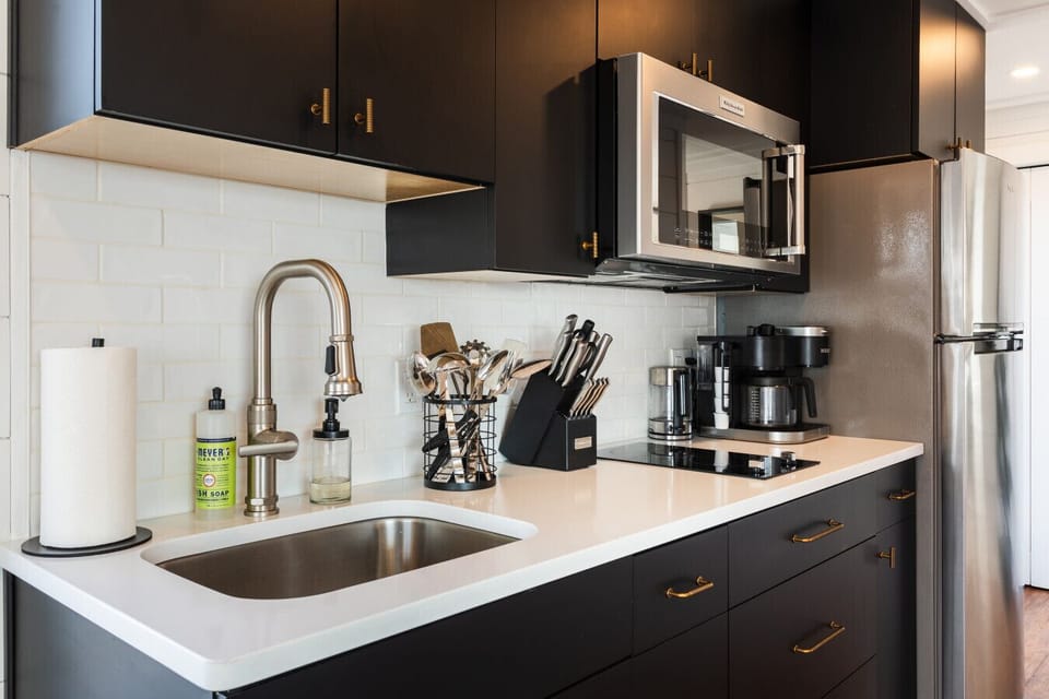 Fully equipped kitchen with Nespresso and drip coffee makers, electric stove top, knife block, KitchenAid microwave, and white quartz countertops.