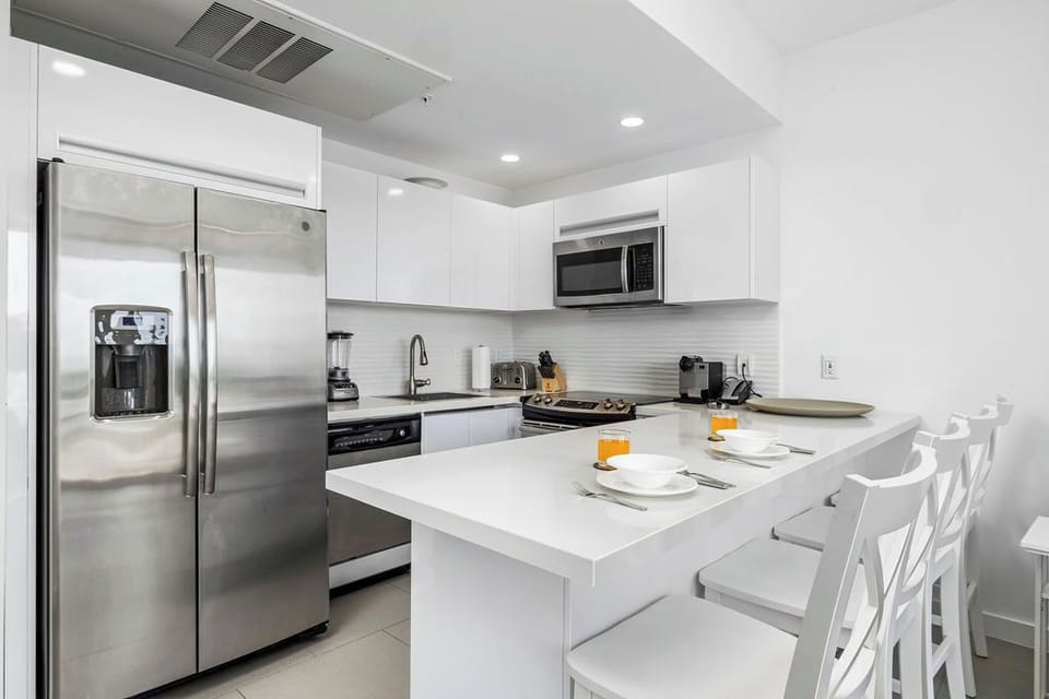 Bright modern kitchen with stainless steel appliances, breakfast bar seating, and everything you need to prepare meals during your stay. The sleek white design offers plenty of counter space for cooking and gathering.