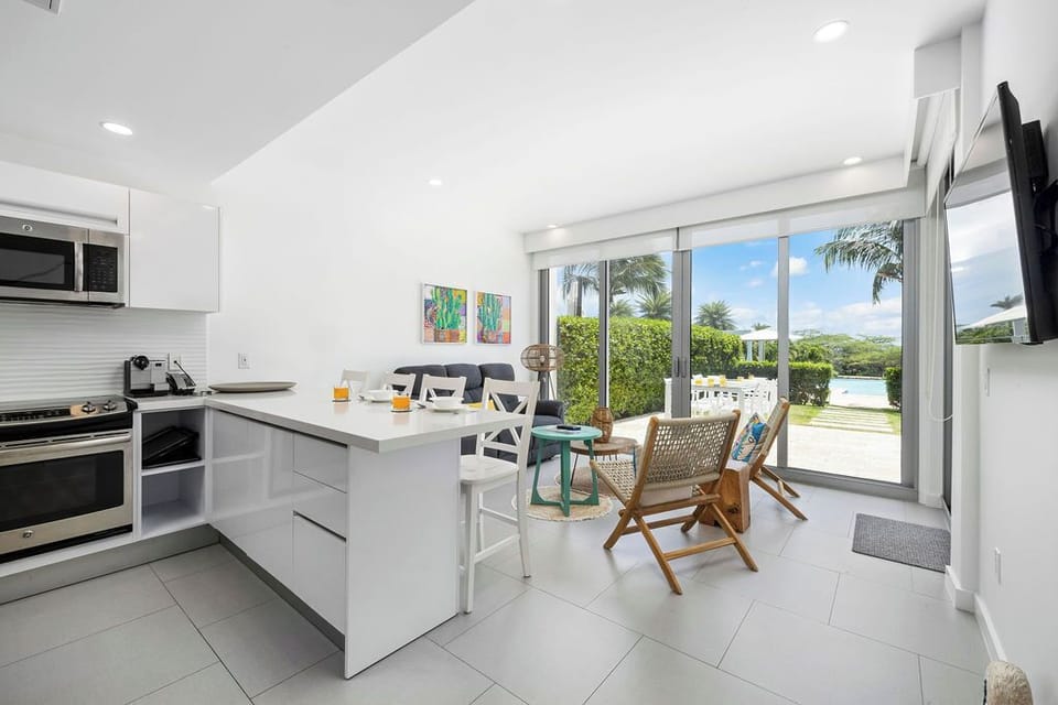 Picture yourself here: a bright, modern kitchen with island seating opens to tropical views and lush greenery just beyond the glass doors, inviting relaxation and outdoor connection.