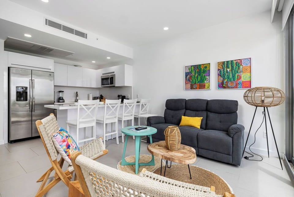 Your open-plan living space blends comfort and style, featuring a plush sofa, vibrant art, and a fully equipped kitchen with breakfast bar seating—perfect for relaxing or gathering.