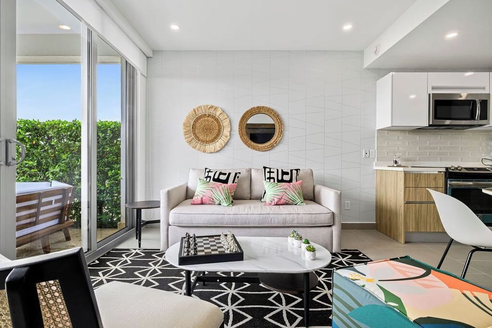 Sink into the plush sofa, enjoy natural light streaming through the glass doors, and unwind in your bright, modern space with a fully-equipped kitchen and tropical balcony view.