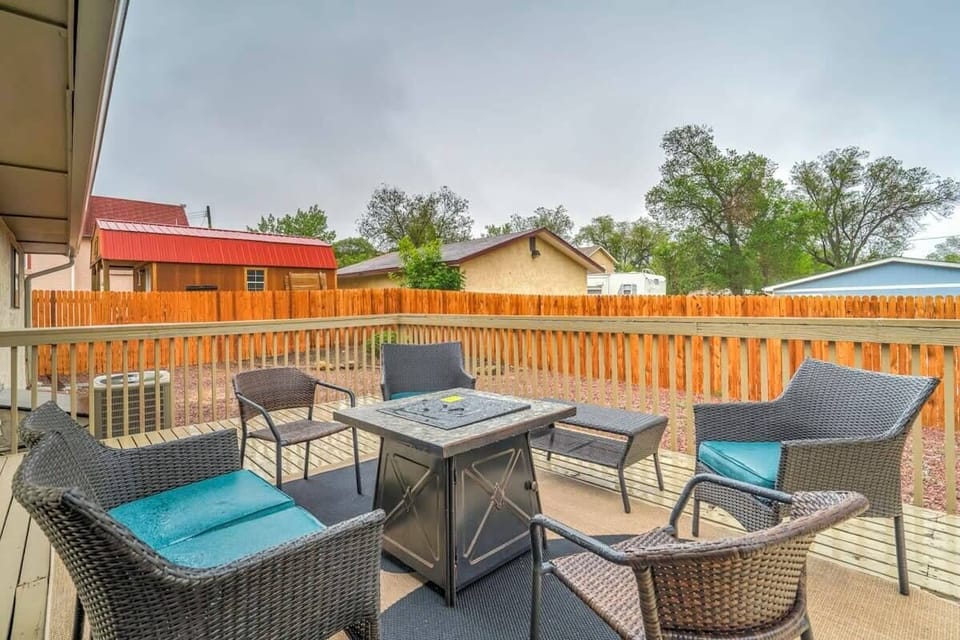 Outdoor patio seating gathered around a square fire table, with cushioned wicker chairs and a wood fence backdrop—an easy spot to sip a drink, chat with friends, or unwind in the open air.
