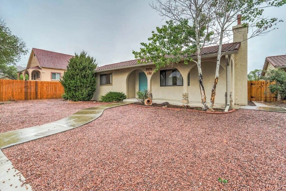 Unit A Main House - Classic stucco home with an arched entry and wide gravel yard—easy arrival, easy lounging. Follow the curved path to the front door beneath tall shade trees.