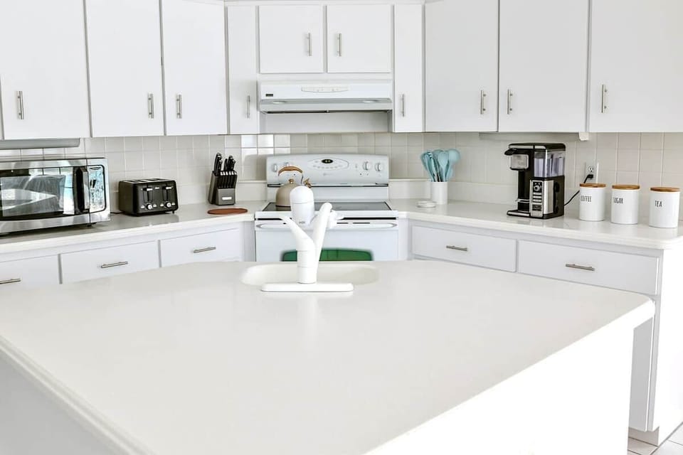 Clean, contemporary kitchen design with white cabinetry, tile backsplash, and essential appliances included.