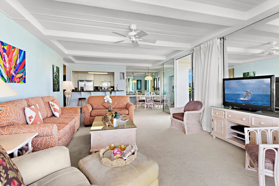 Expansive living area featuring coordinated seating, a pull-out sofa bed, coffered ceilings, and seamless flow to a view-filled lanai.