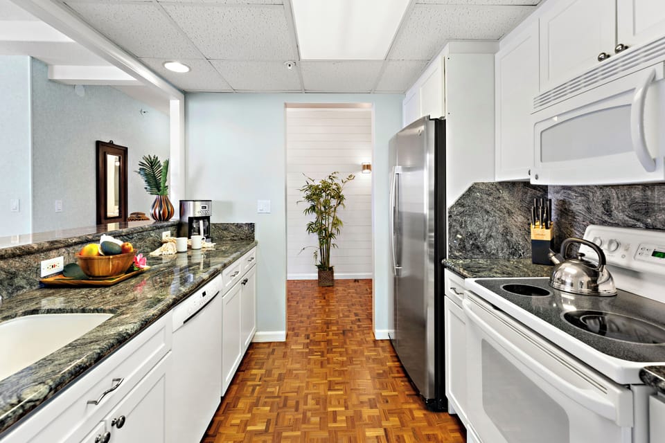 Sleek galley kitchen featuring granite countertops, white cabinetry, stainless steel appliances, and warm wood flooring for a clean, functional layout.