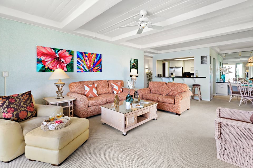 Well-appointed living space with plush furnishings, bold island artwork, and a central coffee table anchoring the open layout.