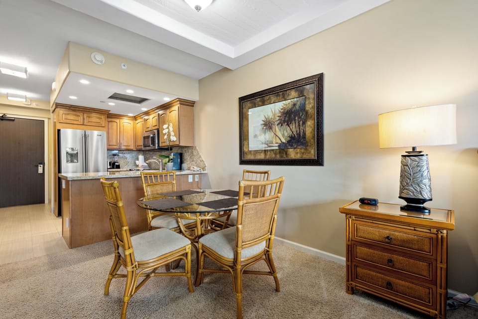 Gather around this inviting dining table where your group can share meals and laughter. The tropical artwork and warm bamboo furnishings create a relaxed island vibe, while the open kitchen nearby makes serving effortless.