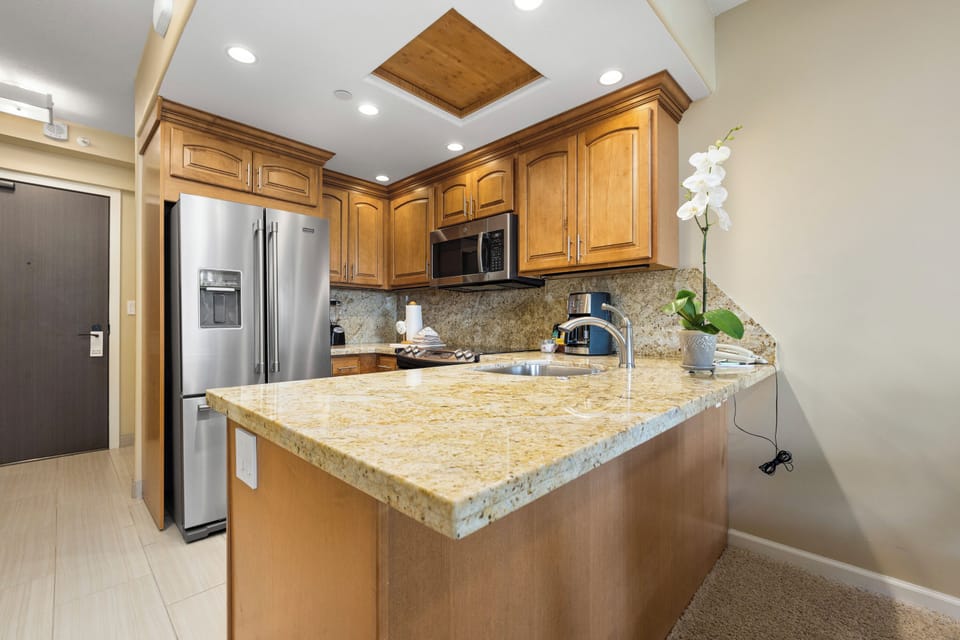 Step into a fully-equipped kitchen where warm wood cabinetry meets modern stainless appliances. Granite countertops provide ample space for meal prep, while recessed lighting and unique ceiling details create an inviting culinary haven.