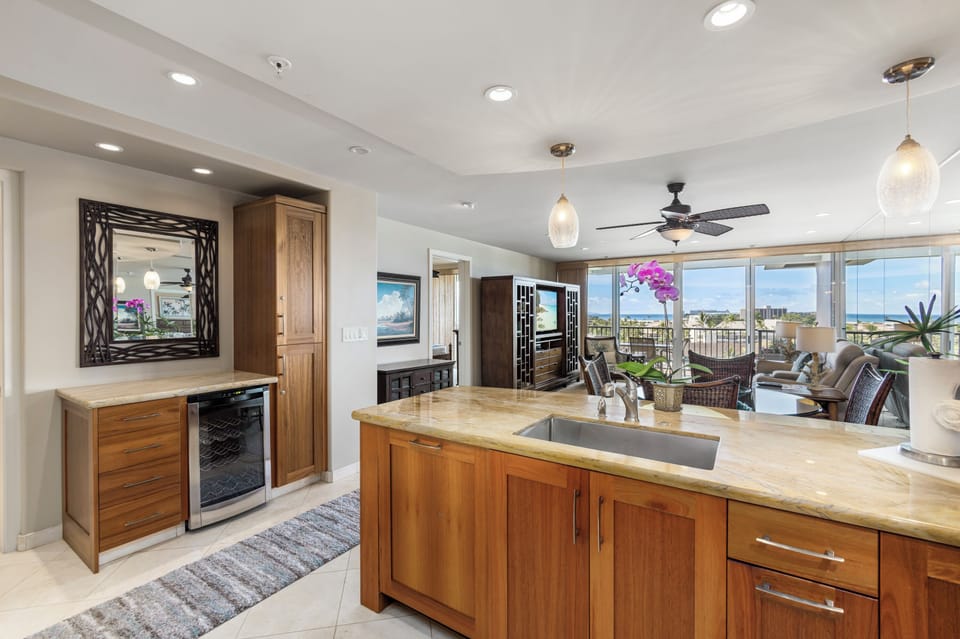 Your spacious, light-filled kitchen opens to a sunny balcony with ocean views—imagine prepping meals against this coastal backdrop, with pendant lights softly glowing overhead.