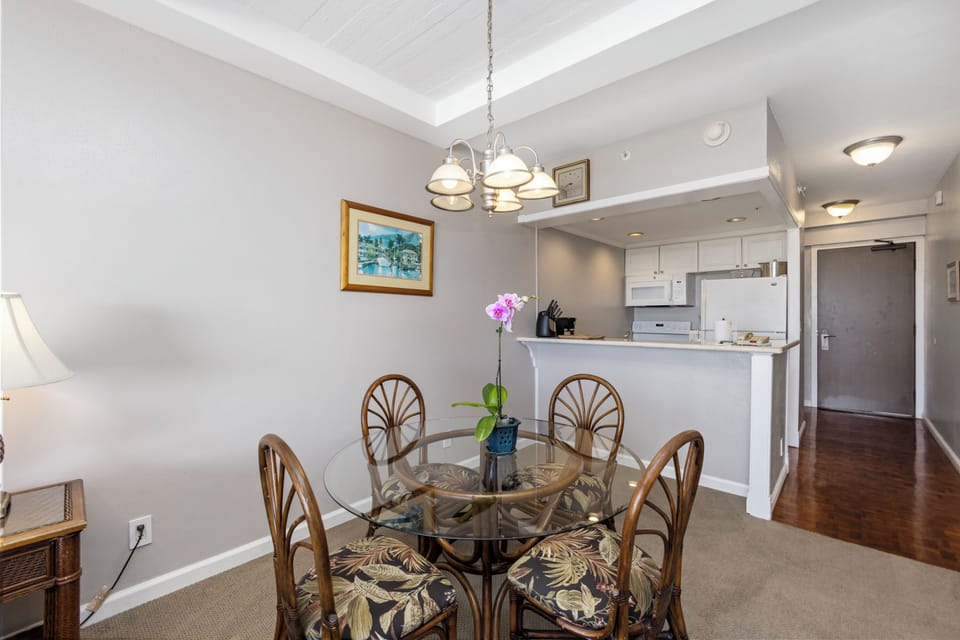Gather around this elegant glass-top dining table for four, perfectly positioned under charming overhead lighting. The open floor plan flows seamlessly into your well-equipped kitchen, ideal for enjoying meals together.