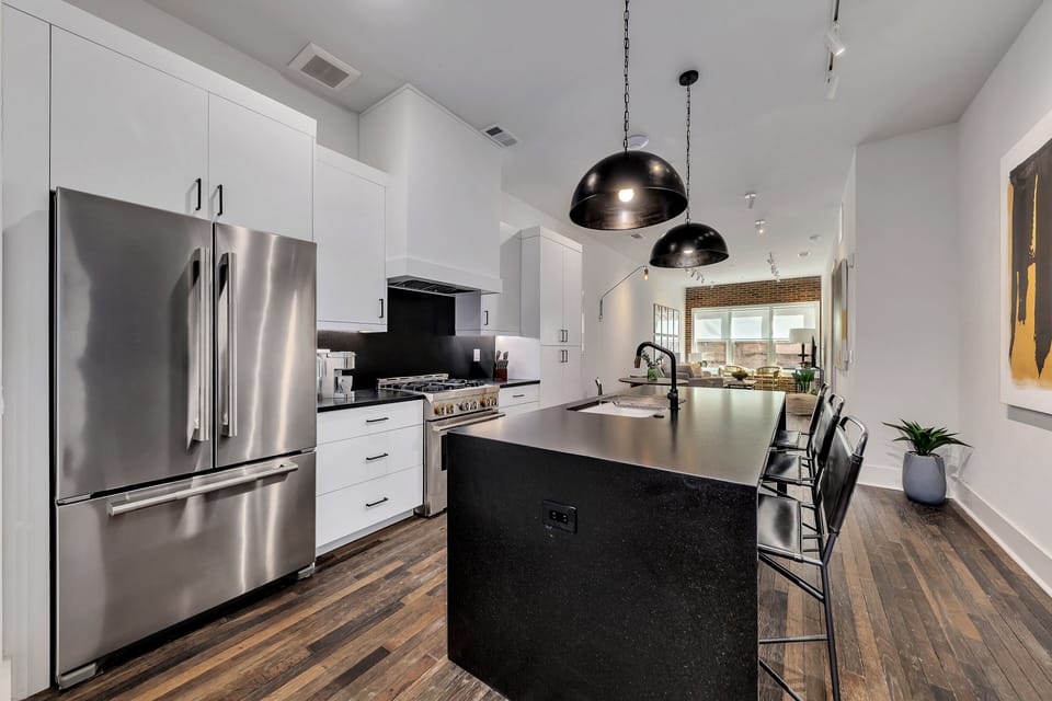 Sleek kitchen w/ stainless steel appliances, large island & modern pendant lighting