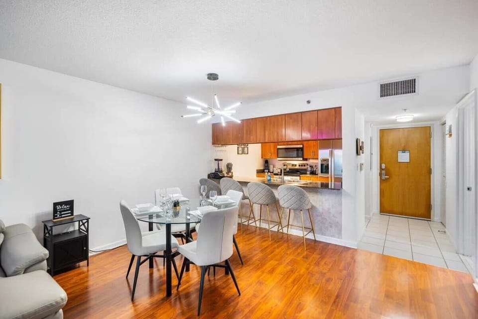 Modern dining area with a glass table and bar seating adjacent to a fully equipped kitchen.