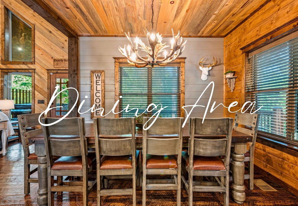 Dining area with a long table, antler chandelier, and 'Welcome' sign creating a homely cabin atmosphere.