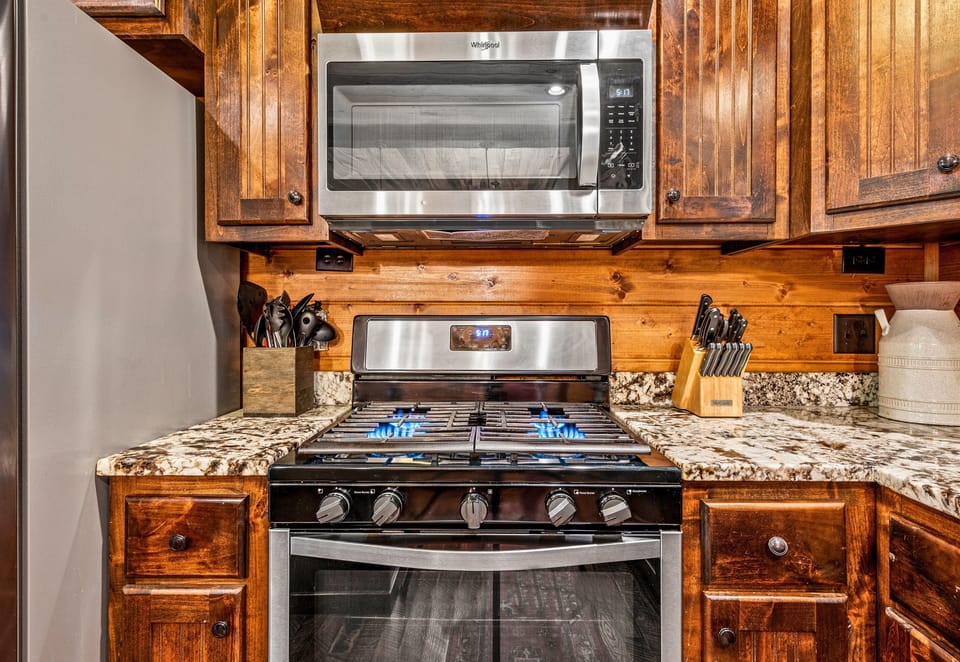 Detail of a well-appointed kitchen with stainless steel gas stove and microwave, set against rich wooden cabinets.