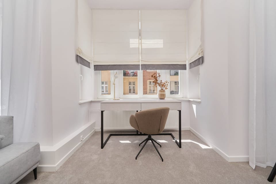 A stylish and minimal workspace with a wooden desk, a chair, and a view out of a large window, offering a bright ambiance.