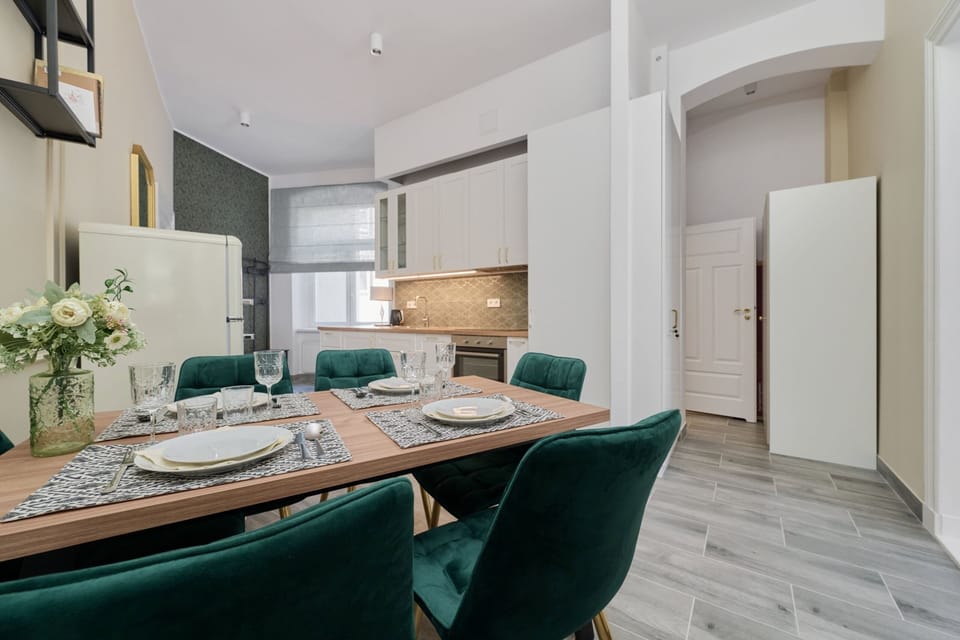 A small dining area with a chic wooden table, velvet green chairs, and modern interior lighting.